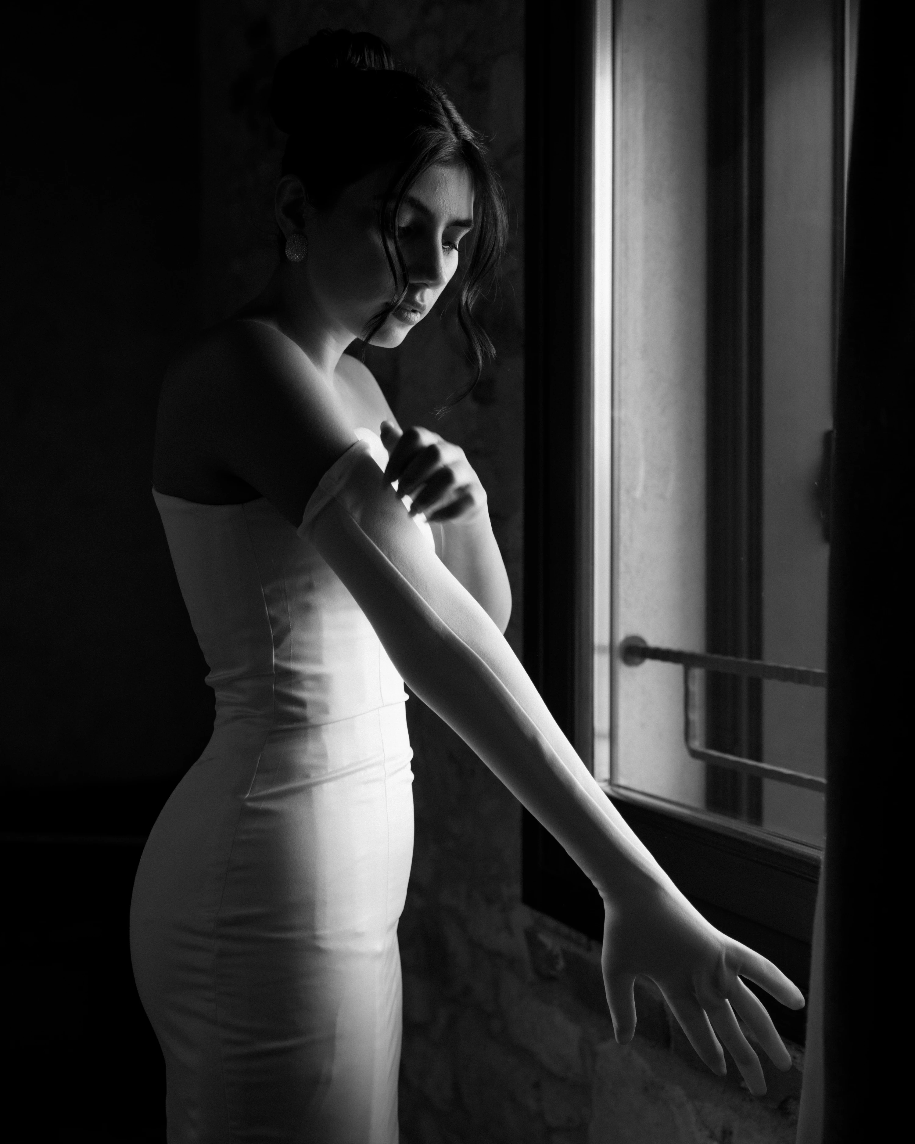 La sposa in controluce davanti a una finestra, il braccio disteso verso la tenda